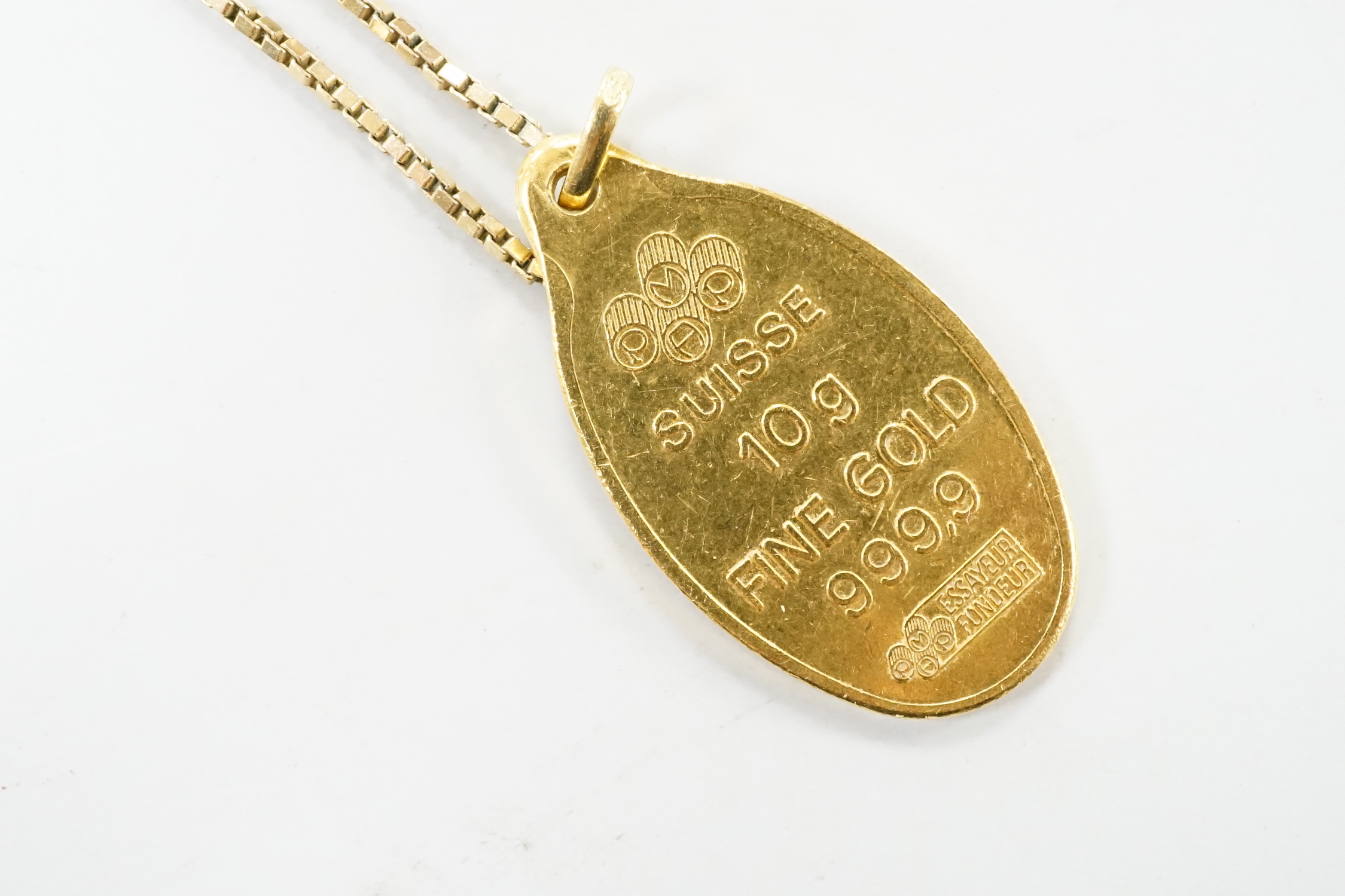 A Suisse 10g yellow metal 'Fine Gold 999.9' oval ingot pendant, on a 9ct gold chain, 3.6 grams.